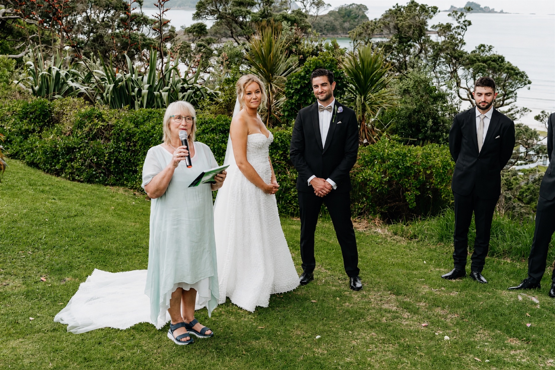 Chris leading a wedding ceremony beside a couple on a coastal lawn