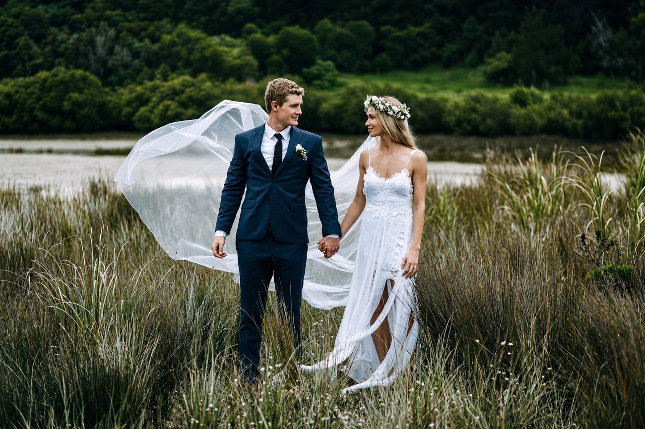 A couple standing in long grass with the veil lifting in the wind
